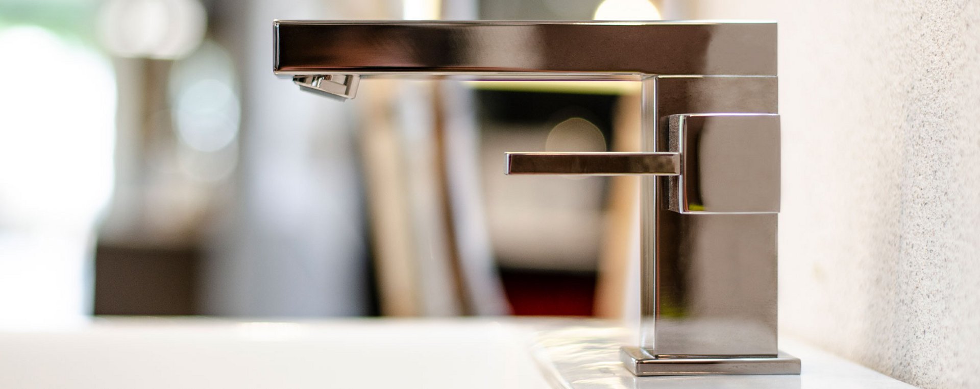 Nahaufnahme einer glänzenden, verchromten Armatur auf einem weißen Waschbecken in einer Badausstellung.