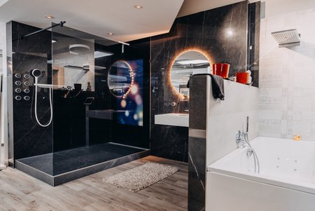 Große Walk-in-Dusche mit schwarzer Marmoroptik und runder LED-Spiegelbeleuchtung, daneben eine weiße Badewanne, helle Wandfliesen und moderne Akzentbeleuchtung.