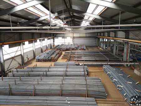 Große Lagerhalle mit zahlreichen Reihen gestapelter Stahlstäbe und -profile, fotografiert von oben.