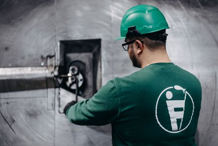 Mitarbeiter mit grünem Helm und Eisen-Fischer Logo auf dem Rücken bedient eine große Metallmaschine.
