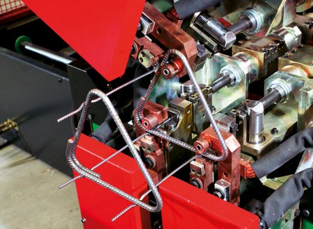 Nahaufnahme einer automatischen Biegemaschine, die aus gerippten Bewehrungsstäben rechtwinklige Bügel für Stahlbeton formt.