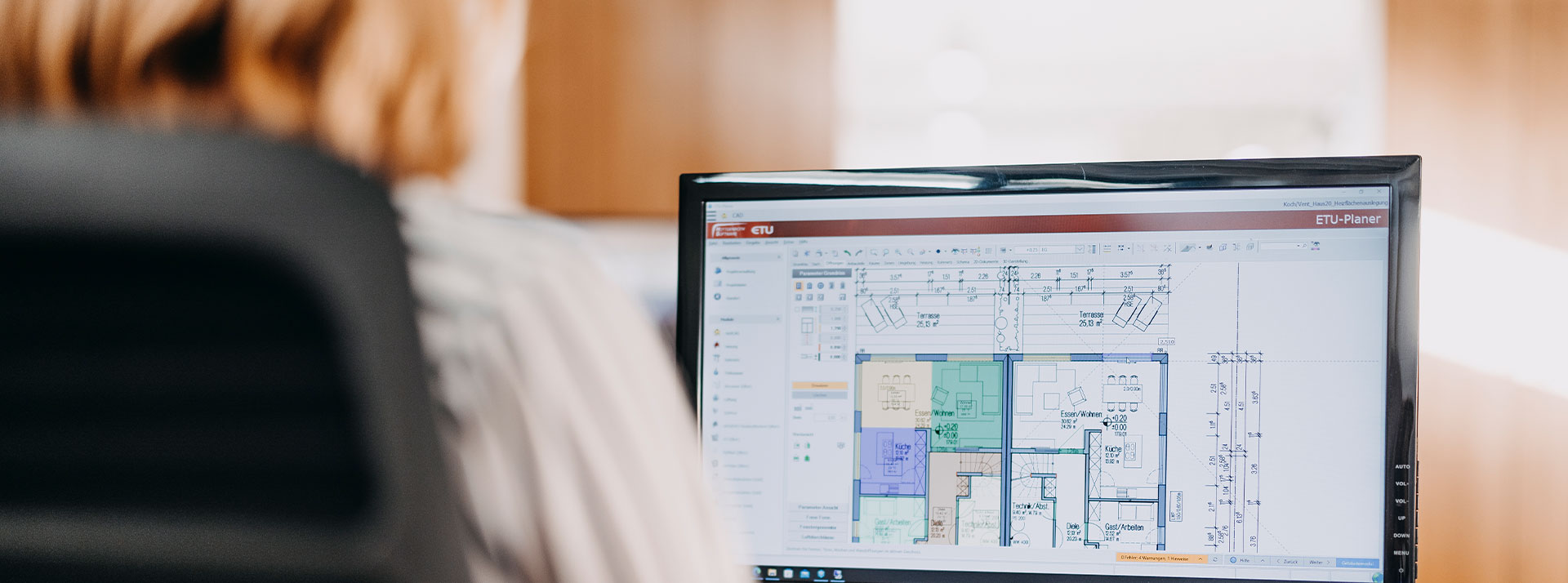 Computerbildschirm zeigt technische Grundrisse in einer Planersoftware, Person arbeitet im Hintergrund.