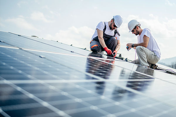 Zwei Techniker installieren Solarmodule auf einem Dach bei sonnigem Wetter.