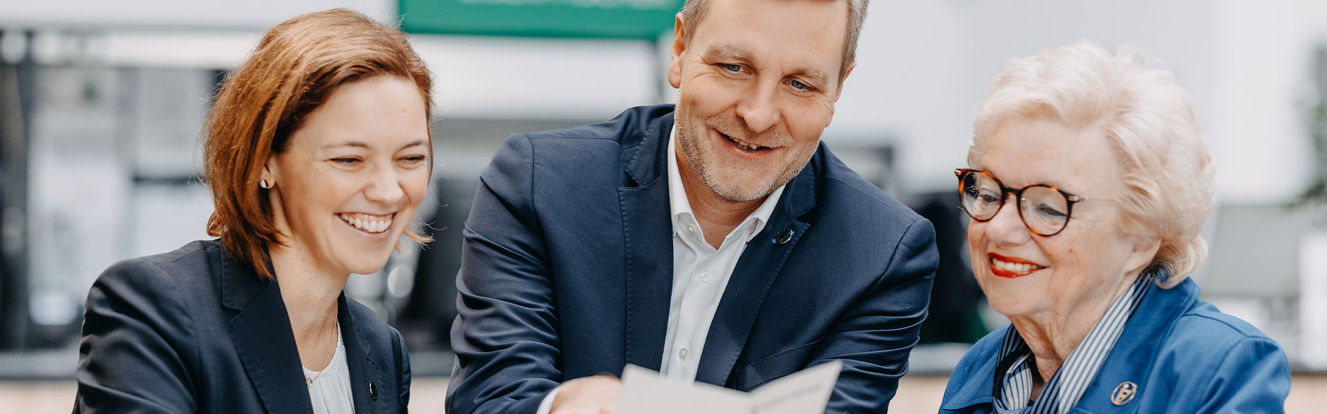 Drei Personen in einem freundlichen Beratungsgespräch, zwei Mitarbeitende und eine Kundin.